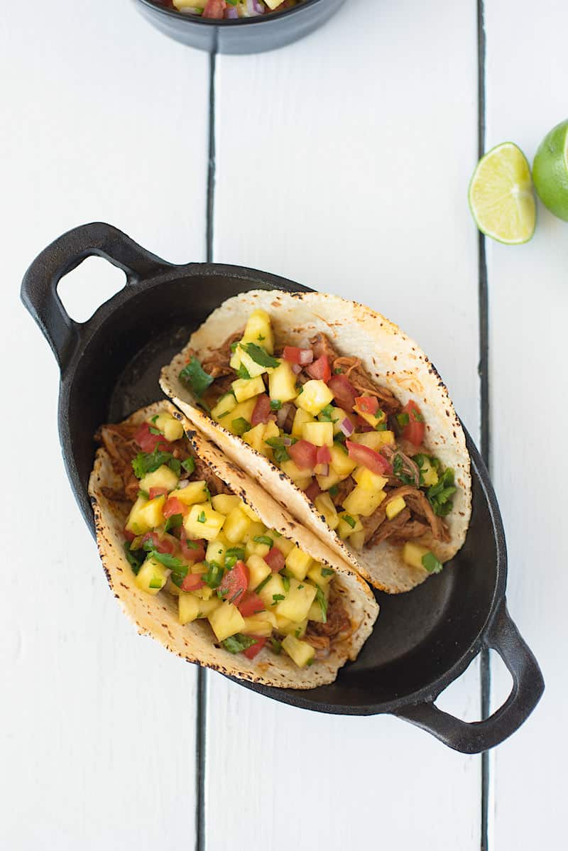 An overhead image of slow cooker pineapple pepper carnitas tacos with fresh lime wedges