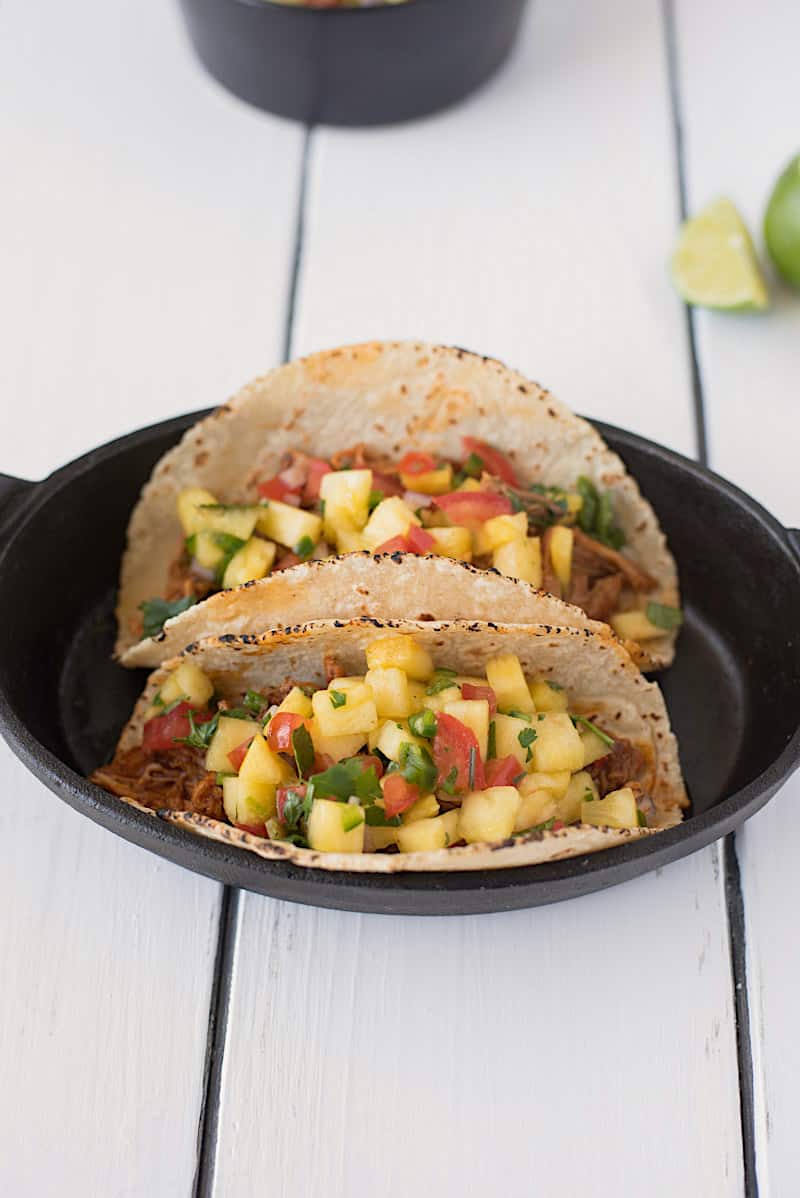 A closeup of slow cooker pineapple pepper carnitas tacos showing the tender pork and fresh pineapple salsa