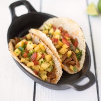 2 carnitas tacos with colorful pineapple salsa in a black bowl