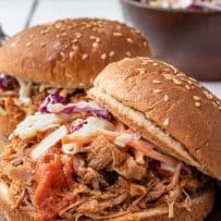 2 sesame buns filled with pulled pork and coleslaw with barbecue sauce dripping out