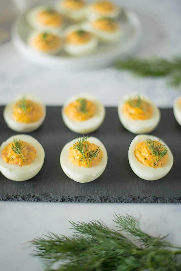 Smoked salmon deviled eggs lined up in 2 rows on a grey slate board with fresh dill