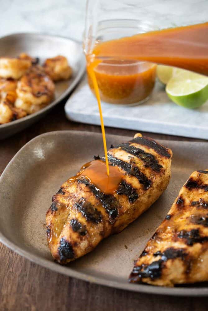 Pouring spicy sauce over grilled chicken