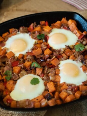 Sweet potatoes, sausage and bacon cooked in a cast iron skillet topped with 4 sunny side up eggs