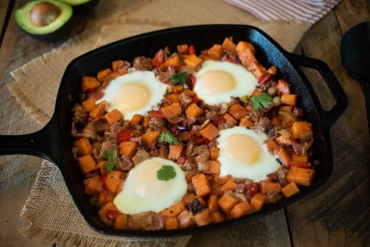 Sweet potatoes, sausage and bacon cooked in a cast iron skillet topped with 4 sunny side up eggs