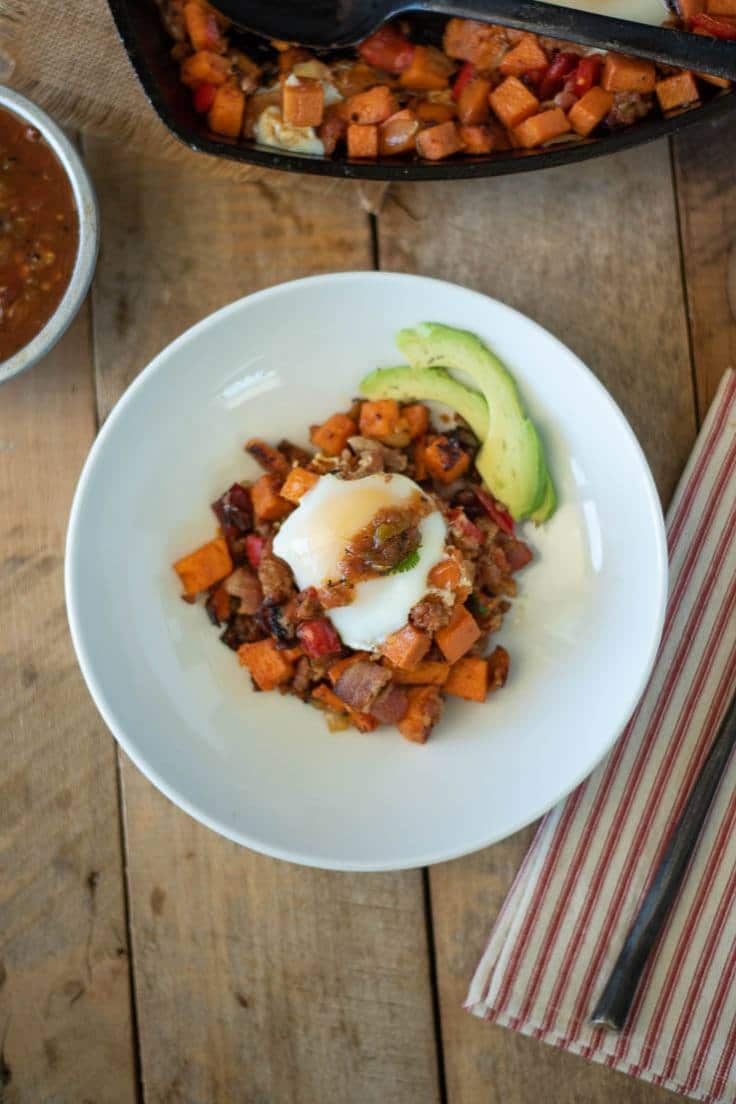 The breakfast skillet is served on a white plate topped with salsa and fresh avocado