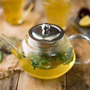 Fresh herbs floating in herbal tea in a clear teapot