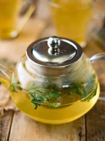 Fresh herbs floating in herbal tea in a clear teapot