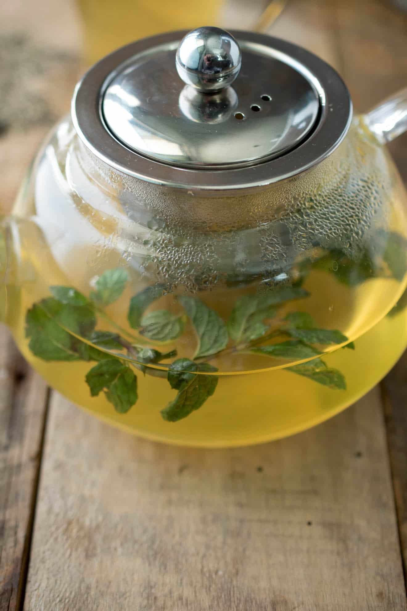 A closeup of soothing therapeutic herbal tea in a glass teapot with fresh herbs