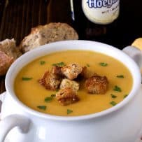 A white soup crock bowl of beer soup topped with croutons and chopped parsley