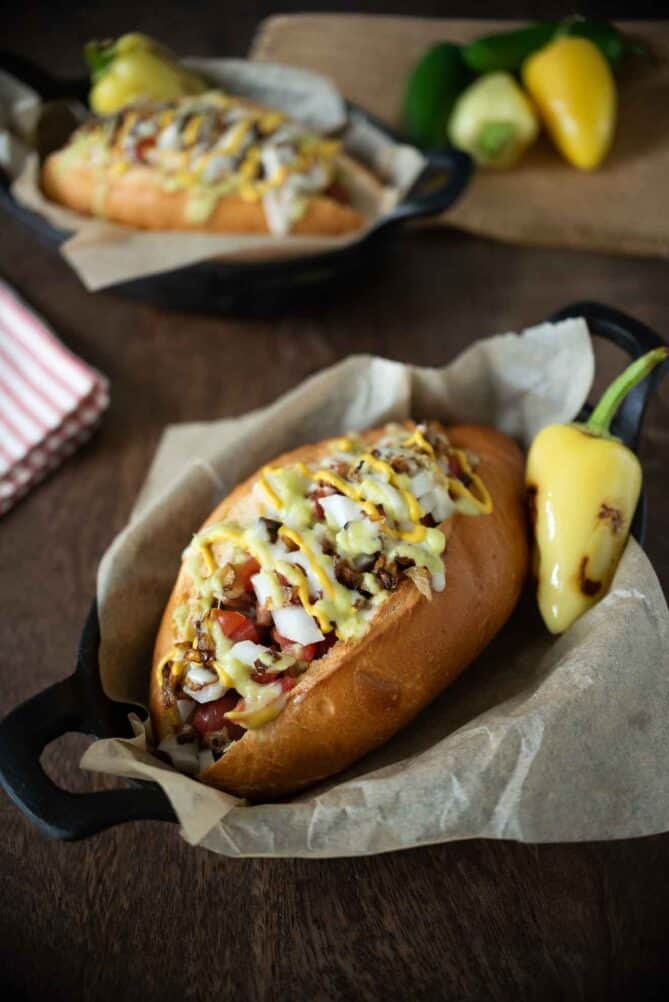 A bacon wrapped hot dog in a bolillo bun with toppings