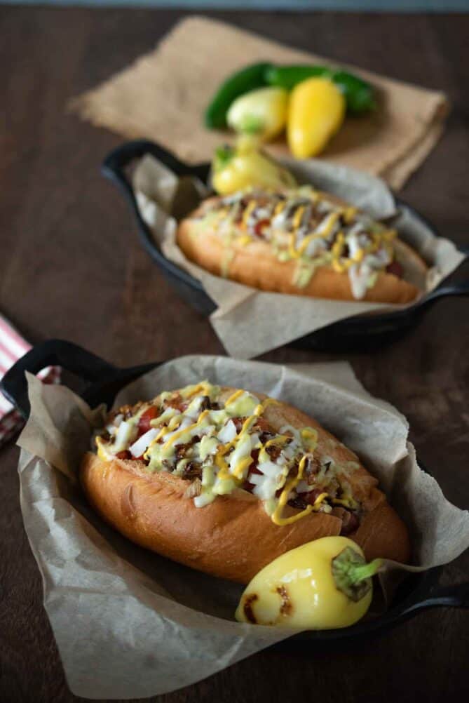 2 Sonoran hot dogs in oval dishes served with pale peppers
