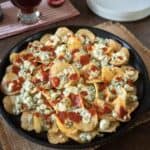 A cast iron skillet filled with potato chips, blue cheese and hot sauce