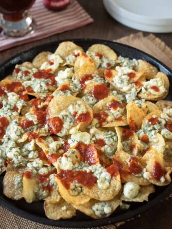 A cast iron skillet filled with potato chips, blue cheese and hot sauce