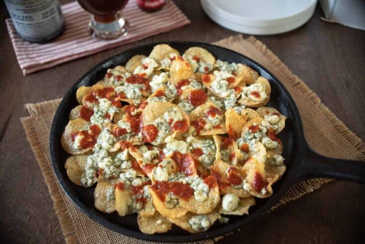 A cast iron skillet filled with potato chips, blue cheese and hot sauce