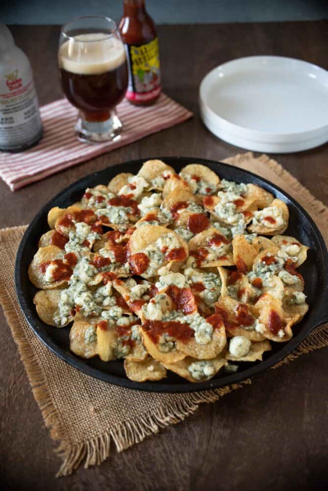 A cast iron platter covered with potato chips topped with melted blue cheese and jalapeño spicy sauce