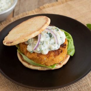 A deliciously browned veggie burger on a naan bun with lettuce topped with raita