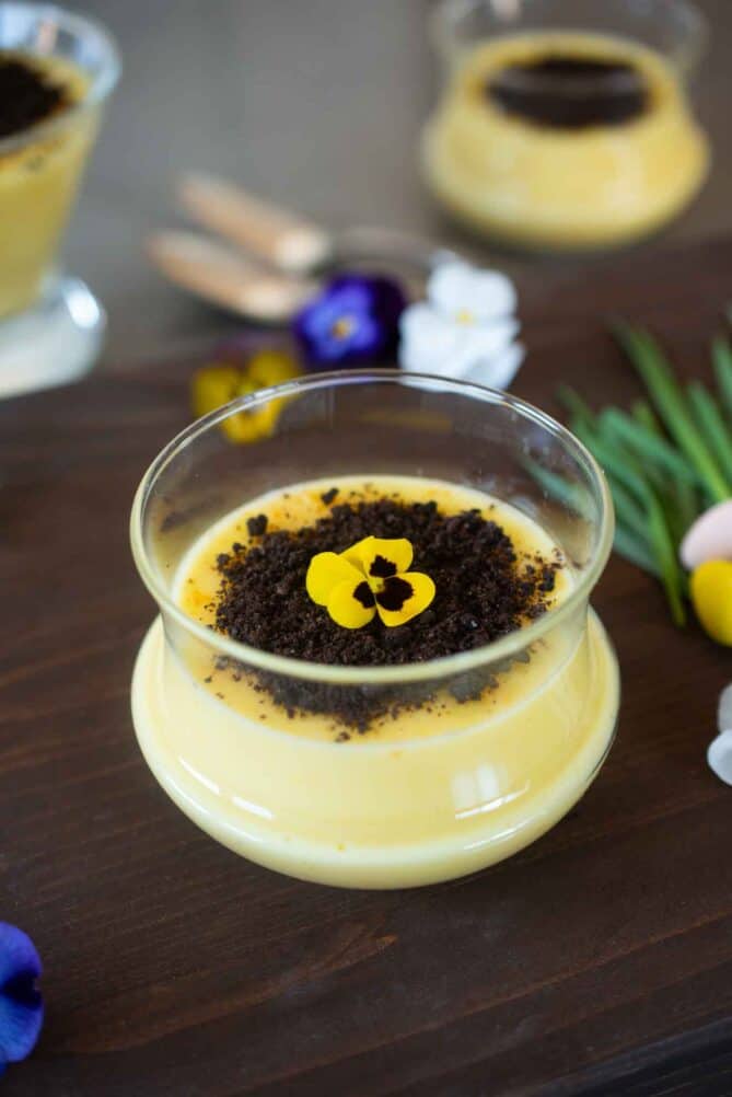 Spring orange custard served in a glass bowl topped with Oreo crumbs and an edible flower