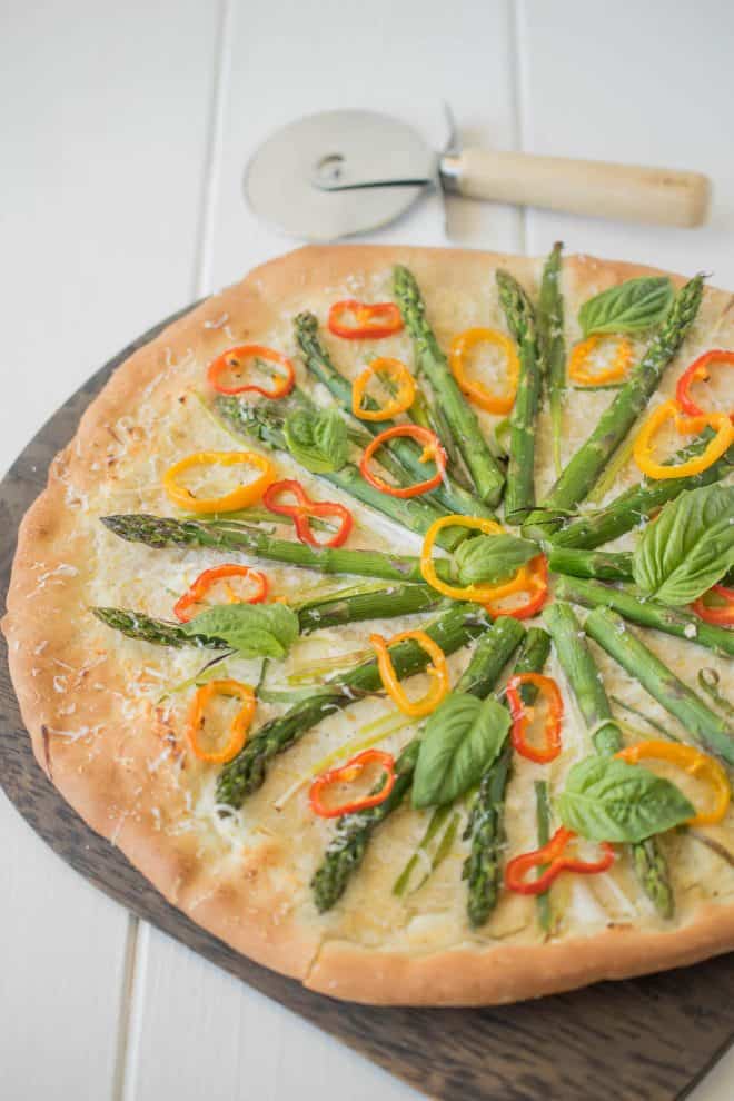 A closeup of asparagus, colorful peppers and basil are the colorful toppings on the pizza