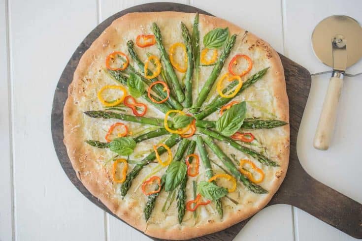 Spring vegetable pizza with colorful vegetables on a pizza board with a pizza cutter
