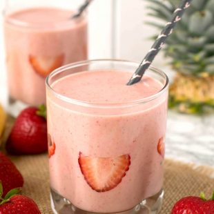 Sliced strawberries decorate the inside of a glass filled with strawberry almond protein power smoothie