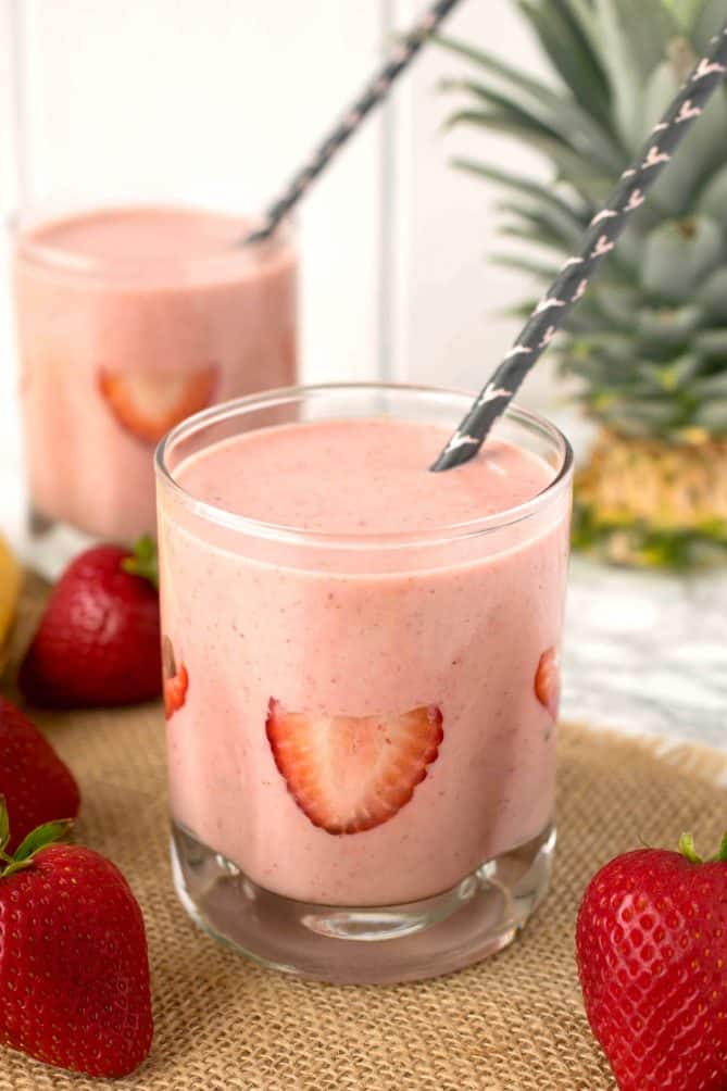 Sliced strawberries decorate the inside of a glass filled with strawberry almond protein power smoothie