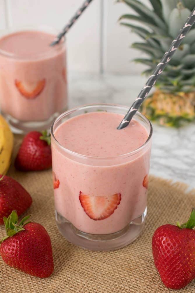 Strawberry smoothie in a glass with a straw and fresh sliced strawberries