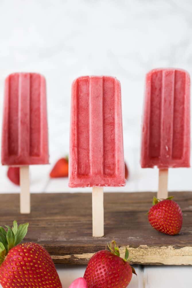 3 strawberry popsicles standing up on a wood board