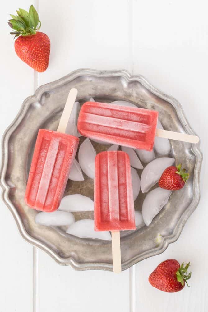 Strawberry popsicles lying down on a plate of ice cubes