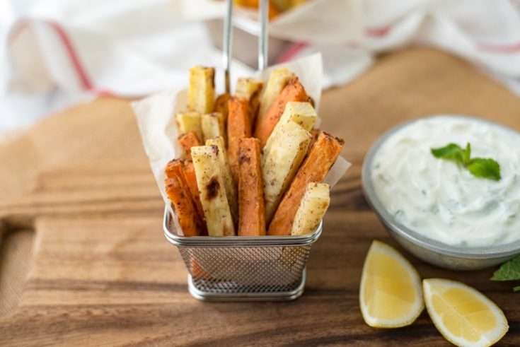 Orange and white baked fries in a basket with yogurt sauce and lemons