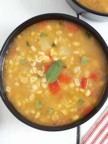 A bowl of sweet corn sage soup garnished with a sage leaf served with bread