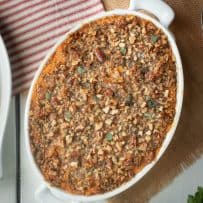 From overhead, an oval baking pan of sweet potato casserole topped with a crumbled pecan topping with butter and sage