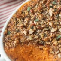 Bright orange sweet potato in a white dish topped with chopped pecans mixed with sage leaves