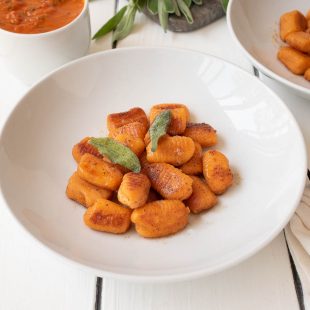 Crispy sweet potato gnocchi served on a white plate with a side of sauce