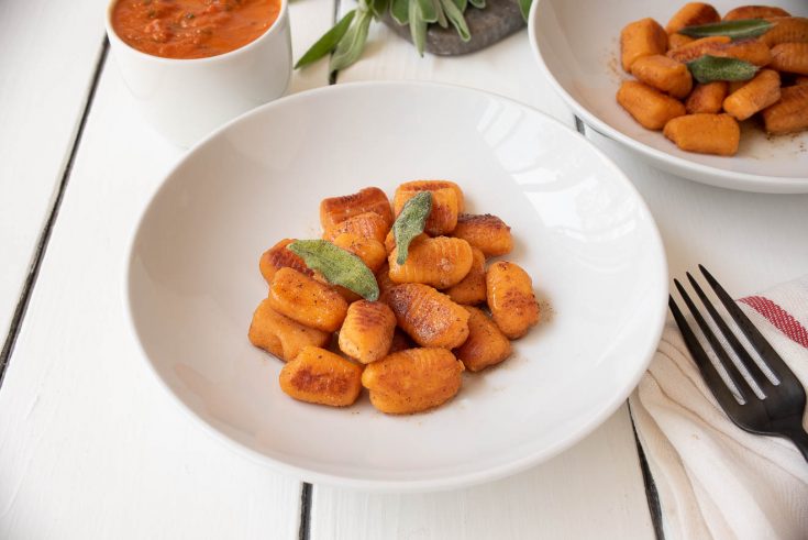 Crispy sweet potato gnocchi served on a white plate with a side of sauce