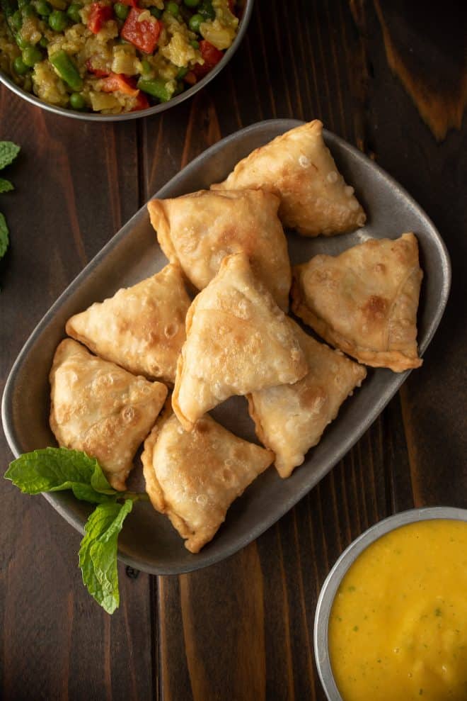 A platter of sweet potato samosas viewed from above with fresh mint