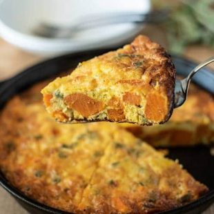 A slice of frittata on a spatula showing the sweet potato and sage inside