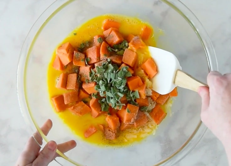 Mixing eggs, sweet potato and sage in a glass bowl