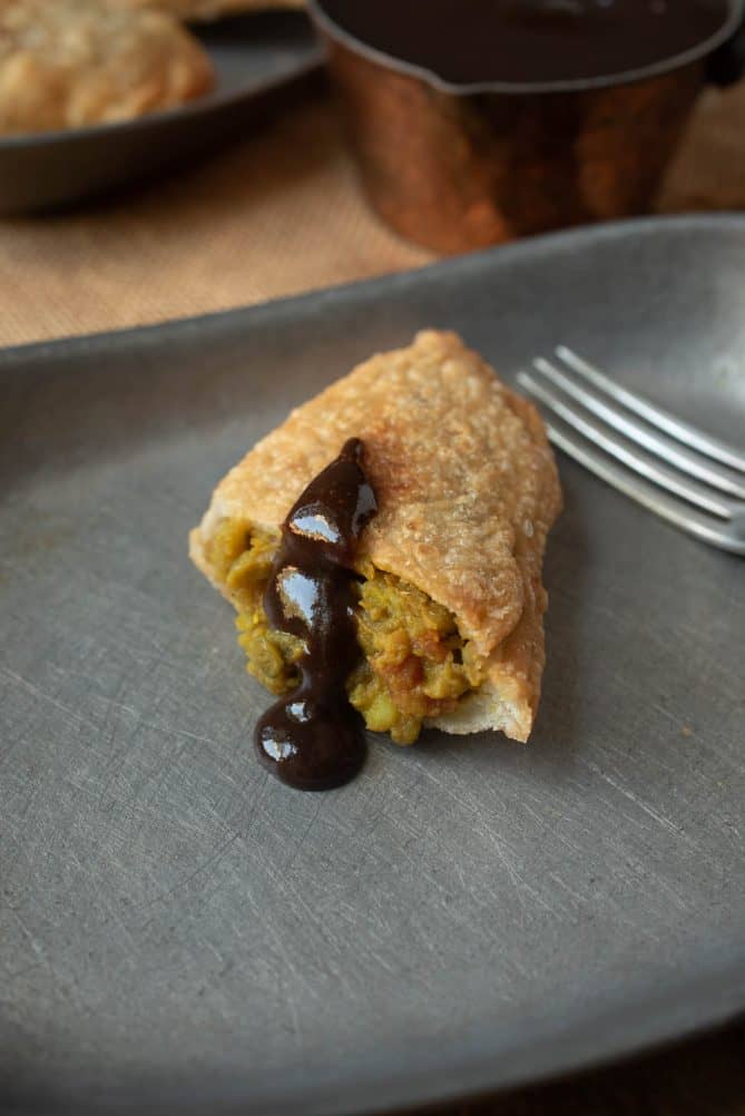 A drizzle of tamarind and date chutney over half of a lentil curry samosa