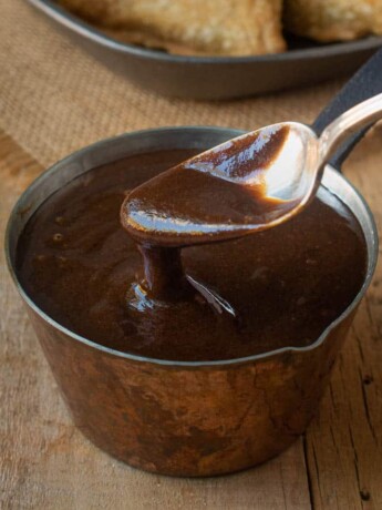 A spoon inside a small pot of tamarind and date chutney