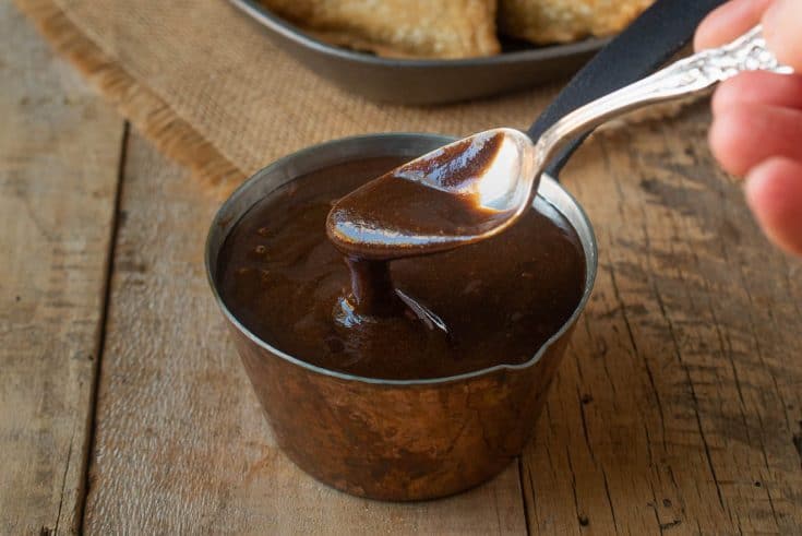 A spoon inside a small pot of tamarind and date chutney