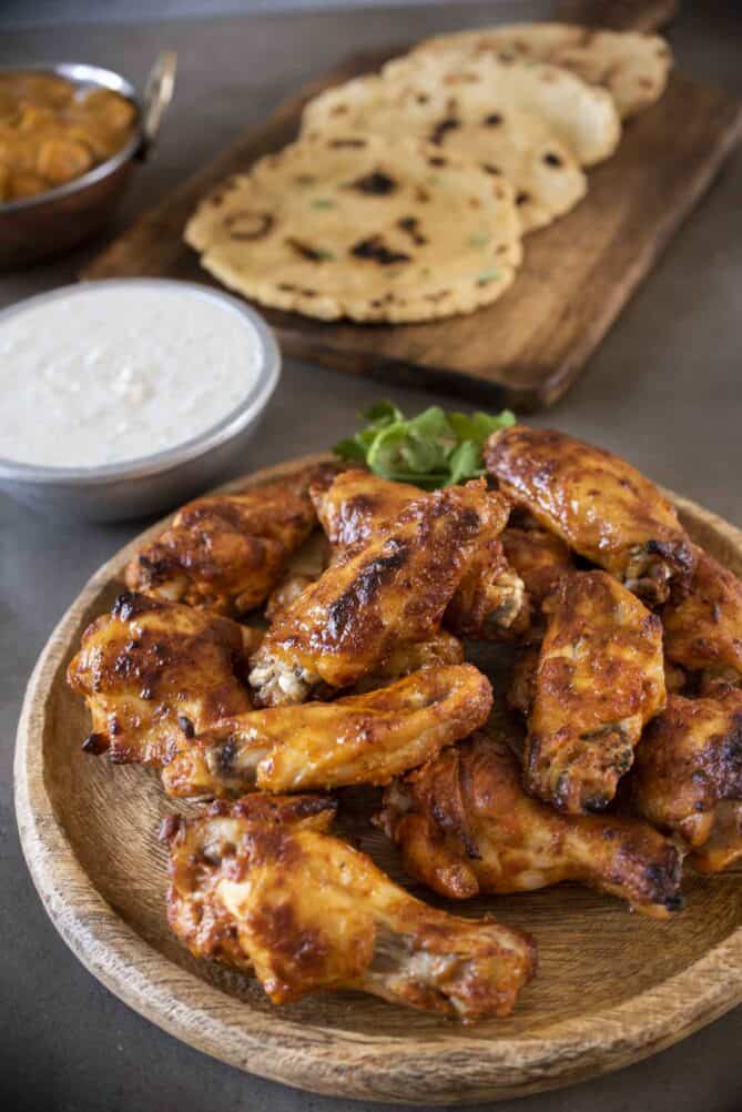 A wooden plate of Indian chicken wings with naan bread