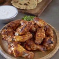 Tandoori masala chicken wings on a serving board with raita
