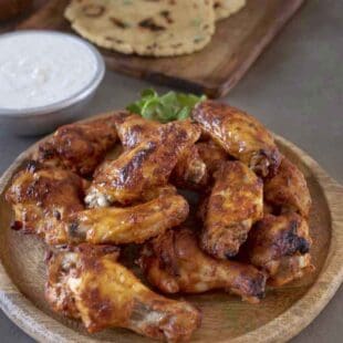 Tandoori masala chicken wings on a serving board with raita