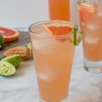A tall glass of tequila Paloma garnished with a wedge of fresh grapefruit and lime rind