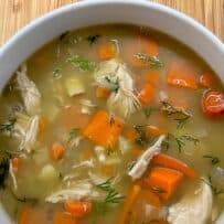 Homemade chicken soup in a white bowl with carrots and potatoes and fresh dill.
