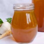 A jar of vegetable stock with vegetables in the background
