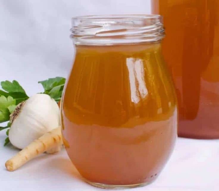 A jar of vegetable stock with vegetables in the background