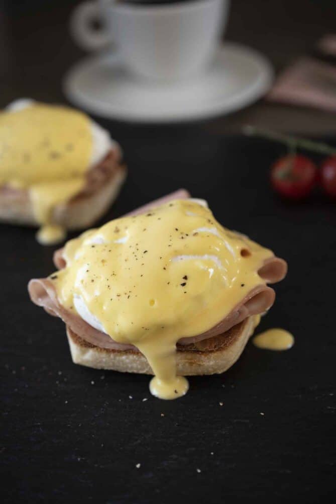 A toasted English muffin topped with sliced mortadella, a poached egg and hollandaise sauce