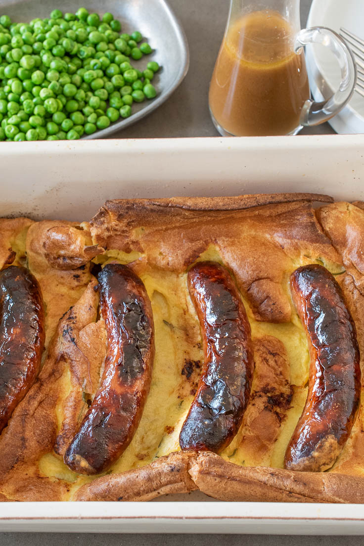 Toad in the hole right out of the oven in a casserole dish with a side of peas and gravy