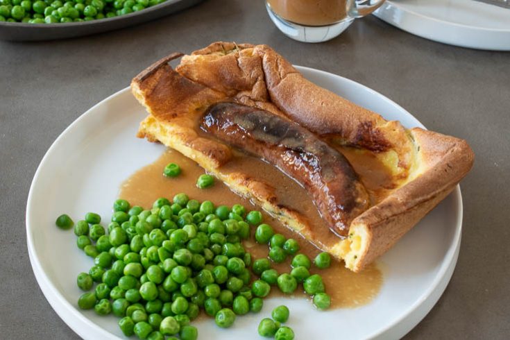 1 toad in the hole sausage inside batter on a white plate with peas and onion gravy